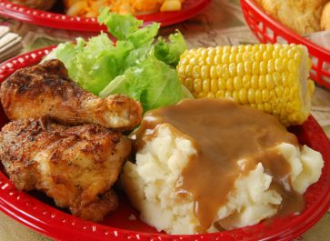 Fried Chicken, Mashed Potatoes, Gravy, Lettuce Salad, Corn On The Cob On Red Plastic Plates