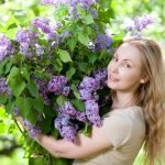 Smiling Blond Lady Holding Huge Bouquet Of Purple Lilacs