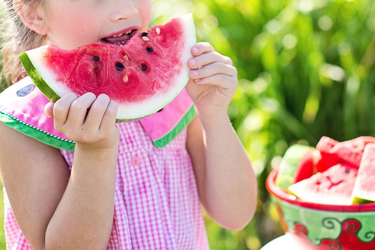 Little Girl in Pink Dress Eating Watermelon in Garden